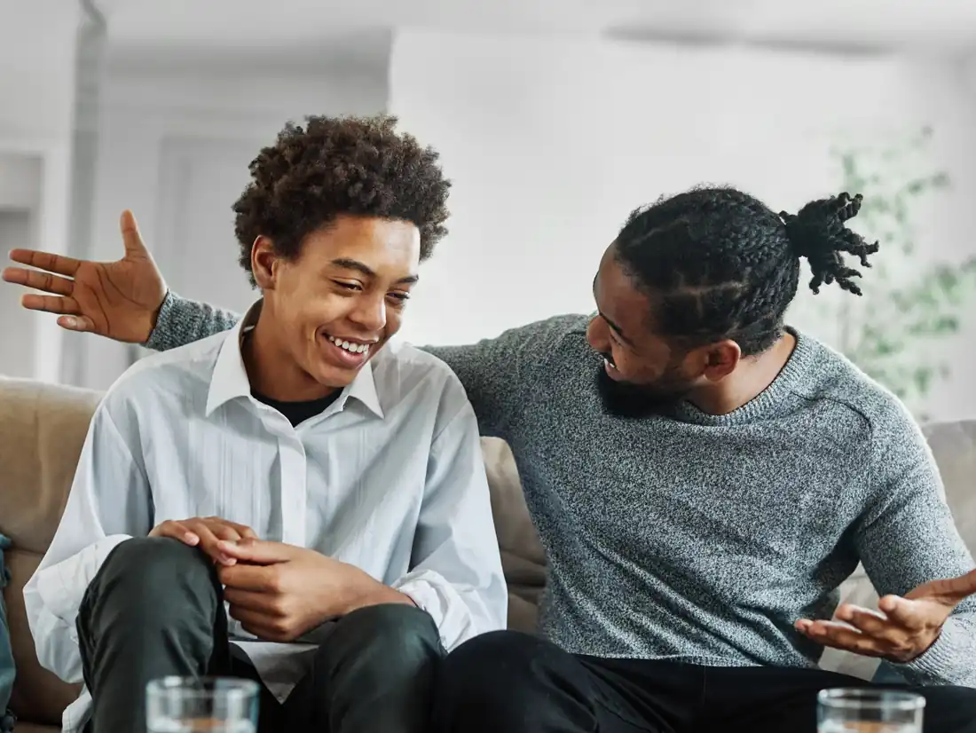 A dad and his teen laughing together on the couch