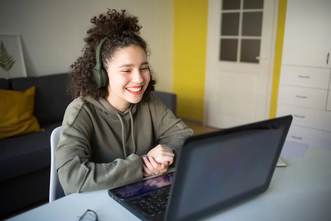 A girl with headphones smiling as she talks on a laptop