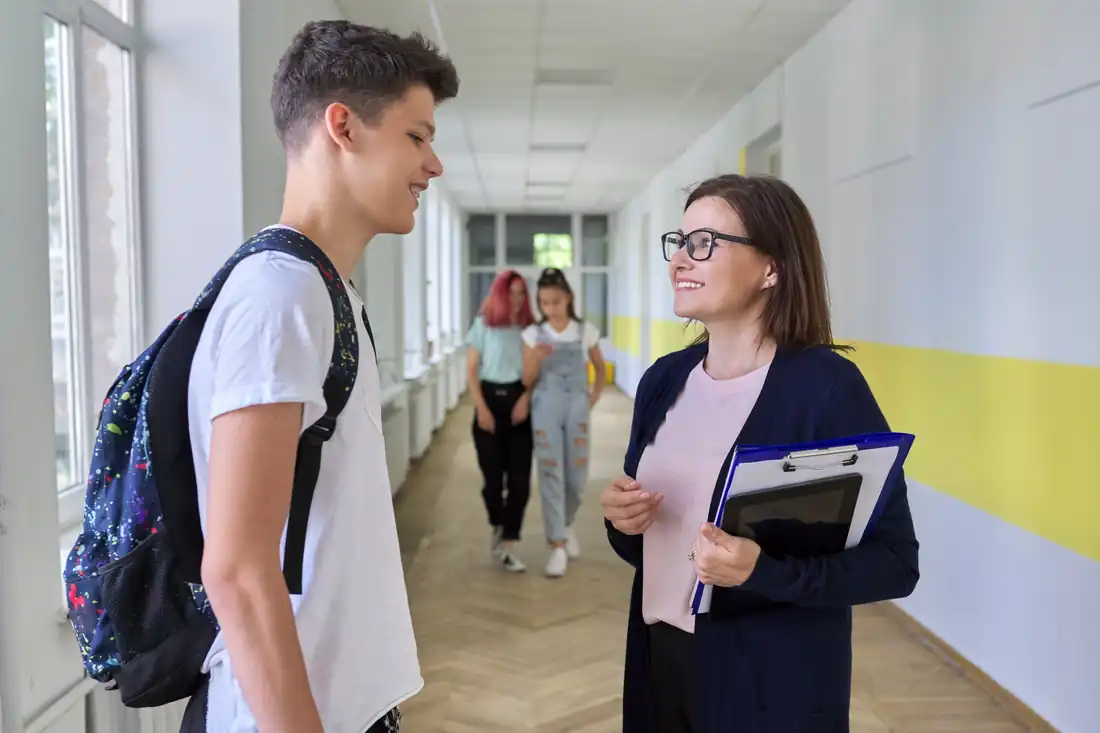 A teen talking with his teacher in the school hallway